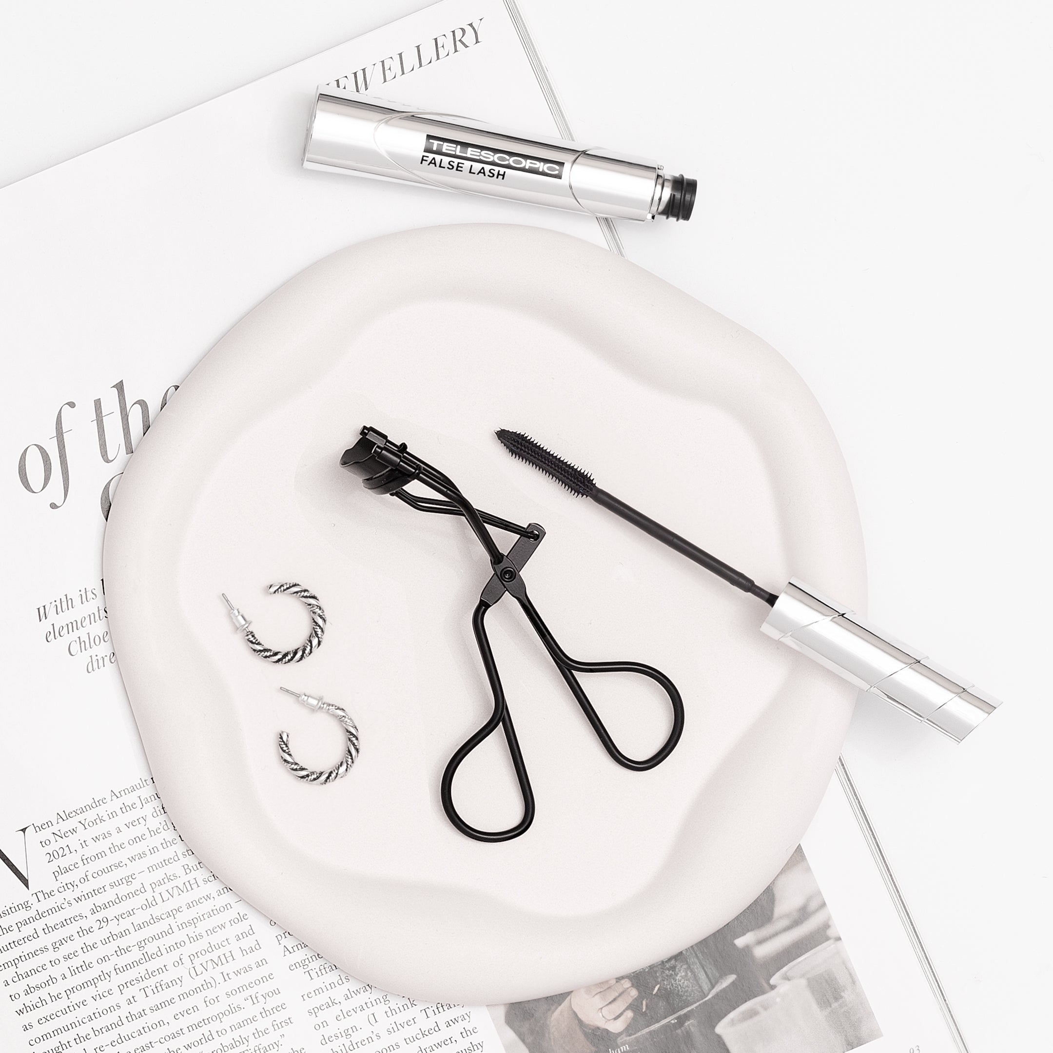 TRUYU Classic Black Eyelash Curler. With Mascara on a plate in front of magazine. Lifestyle photo.
