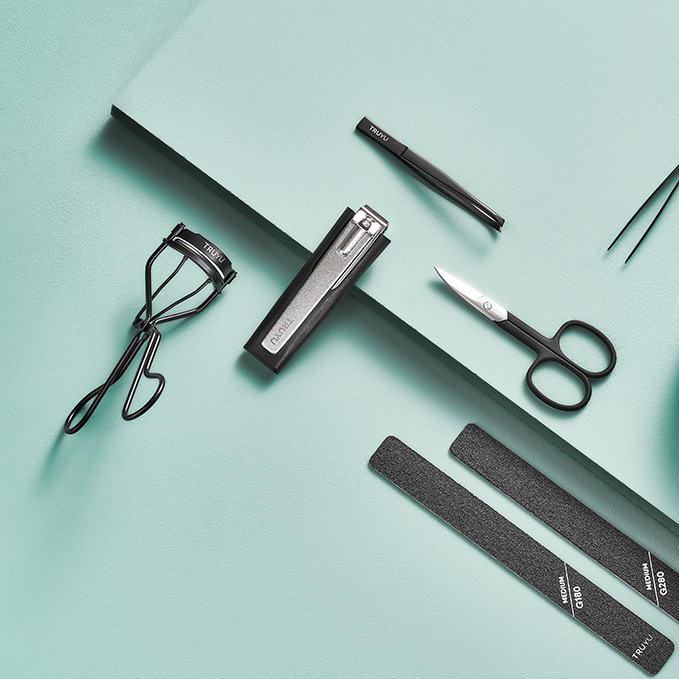 TRUYU black manicure tools on light mint coloured background. Showing Eyelash Curler, Slant Tip Tweezers, Point Tip Tweezers, Nail Scissors, Nail Files and Toenail Clipper & Catcher