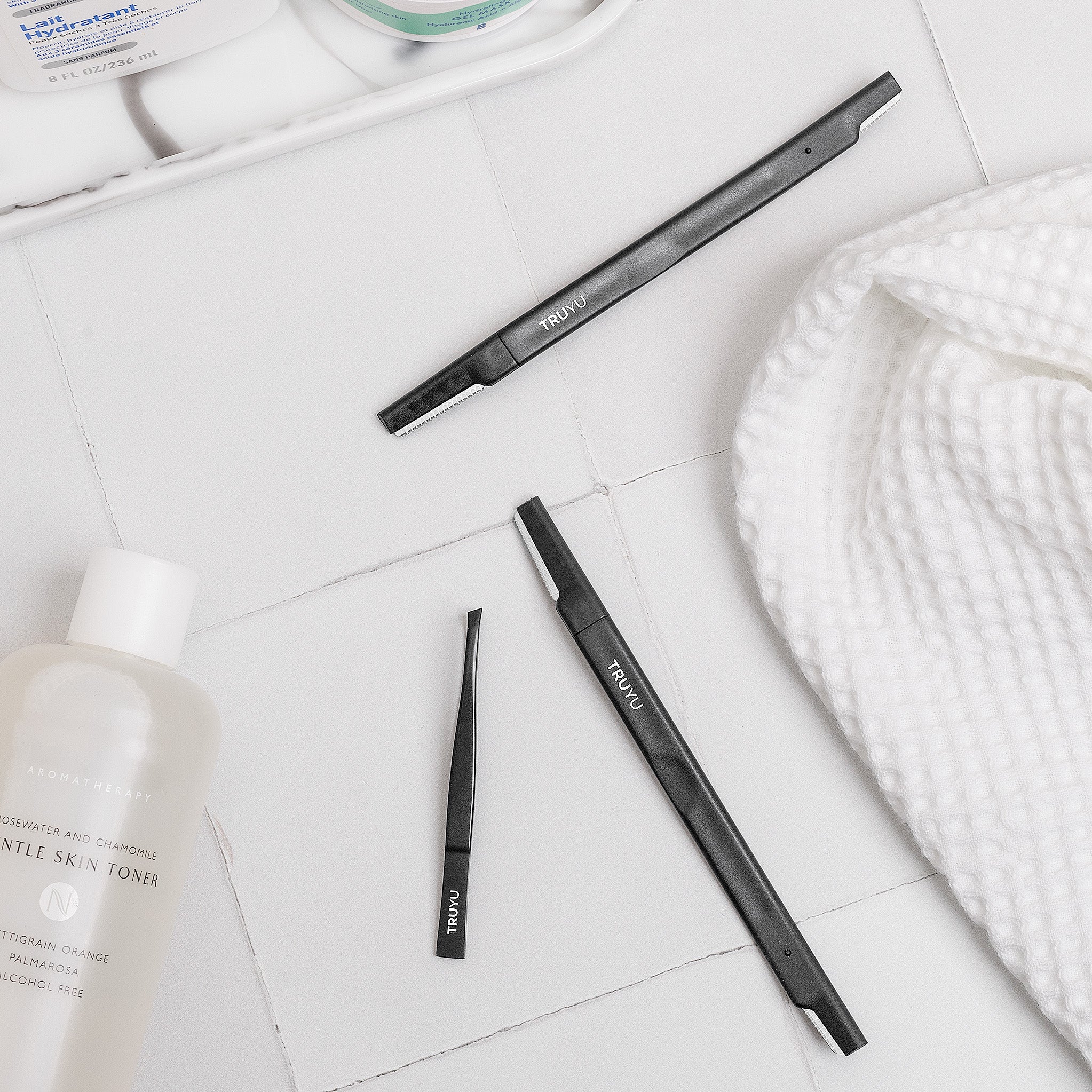 TRUYU Black Facial Razors on bathroom tiles with Slant tip tweezer and towel.