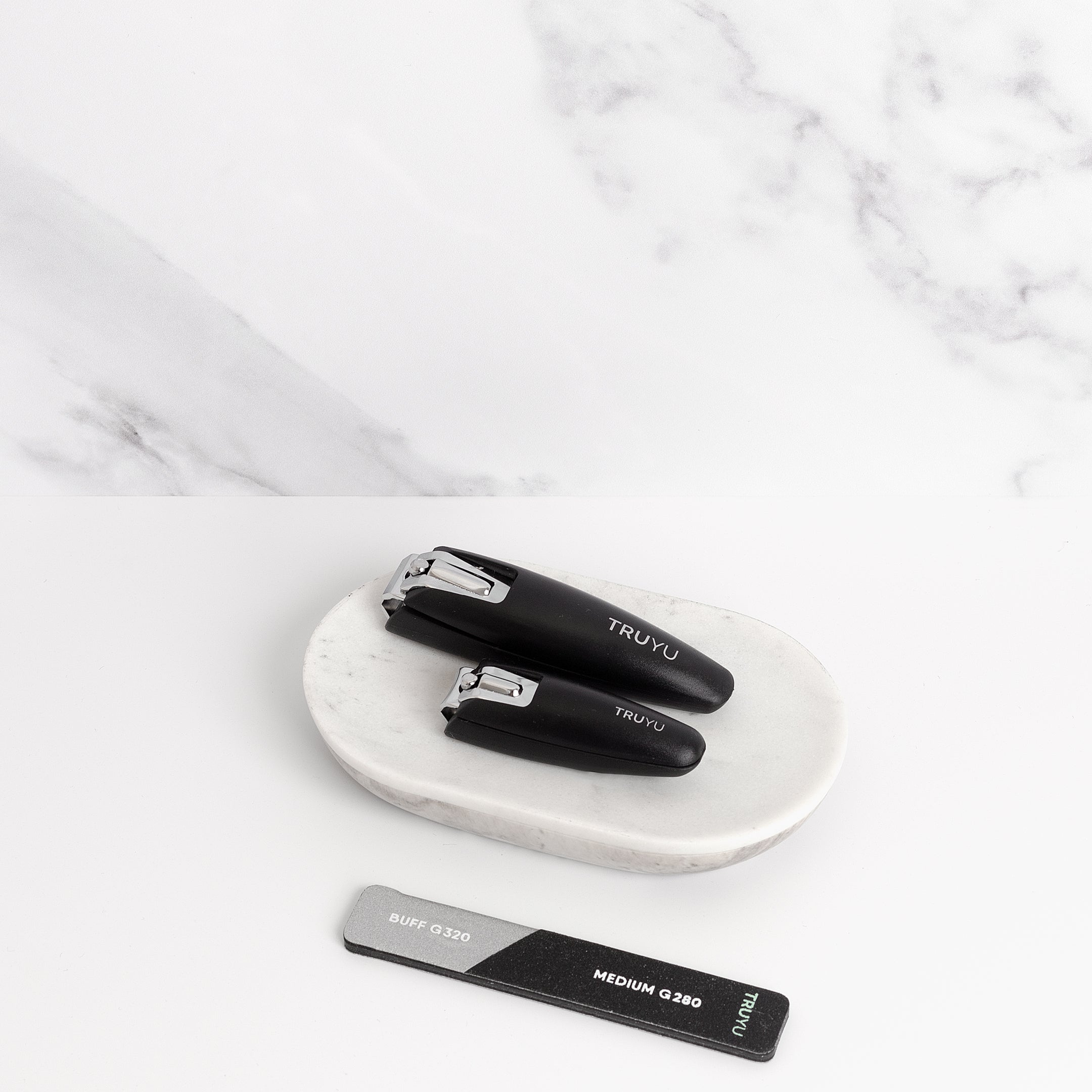 TRUYU Pro Manicure Set, Nail Clipper, Toenail Clipper and Mini Buffer and Nail File. out of pack on a marble background and dish.