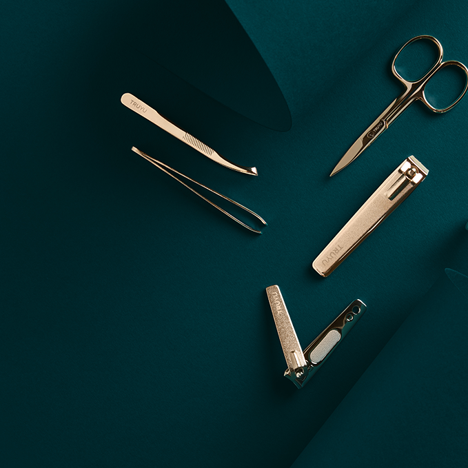 Set of TRUYU Gold Tools on dark green background. Includes, Gold Slant Tip Tweezer, Gold Easy View Tweezer, Gold Nail Scissors, Gold Toenail Clipper and Gold Fingernail Clipper.  