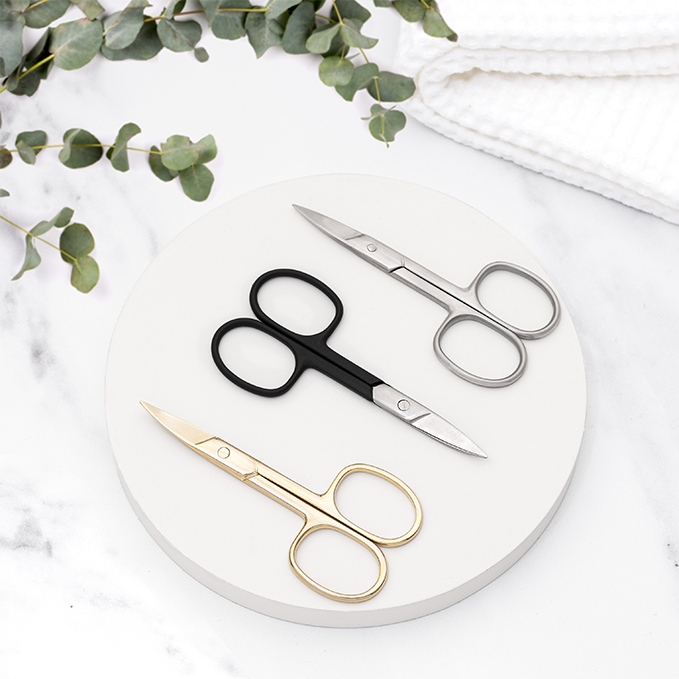 Lifestyle image of three pairs of TRUYU scissors in black, gold, and silver on a white marble surface with green leaves and white towel in background. 