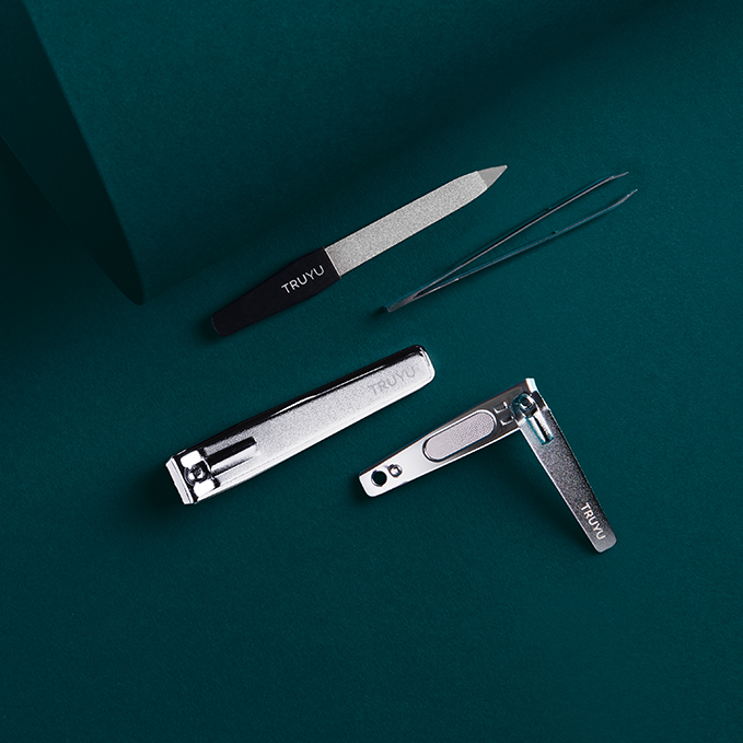TRUYU manicure tools on dark teal background. Showing Straight Toenail Clippers, Sapphire File, Slant Tip Tweezer and open Fingernail Clippers.