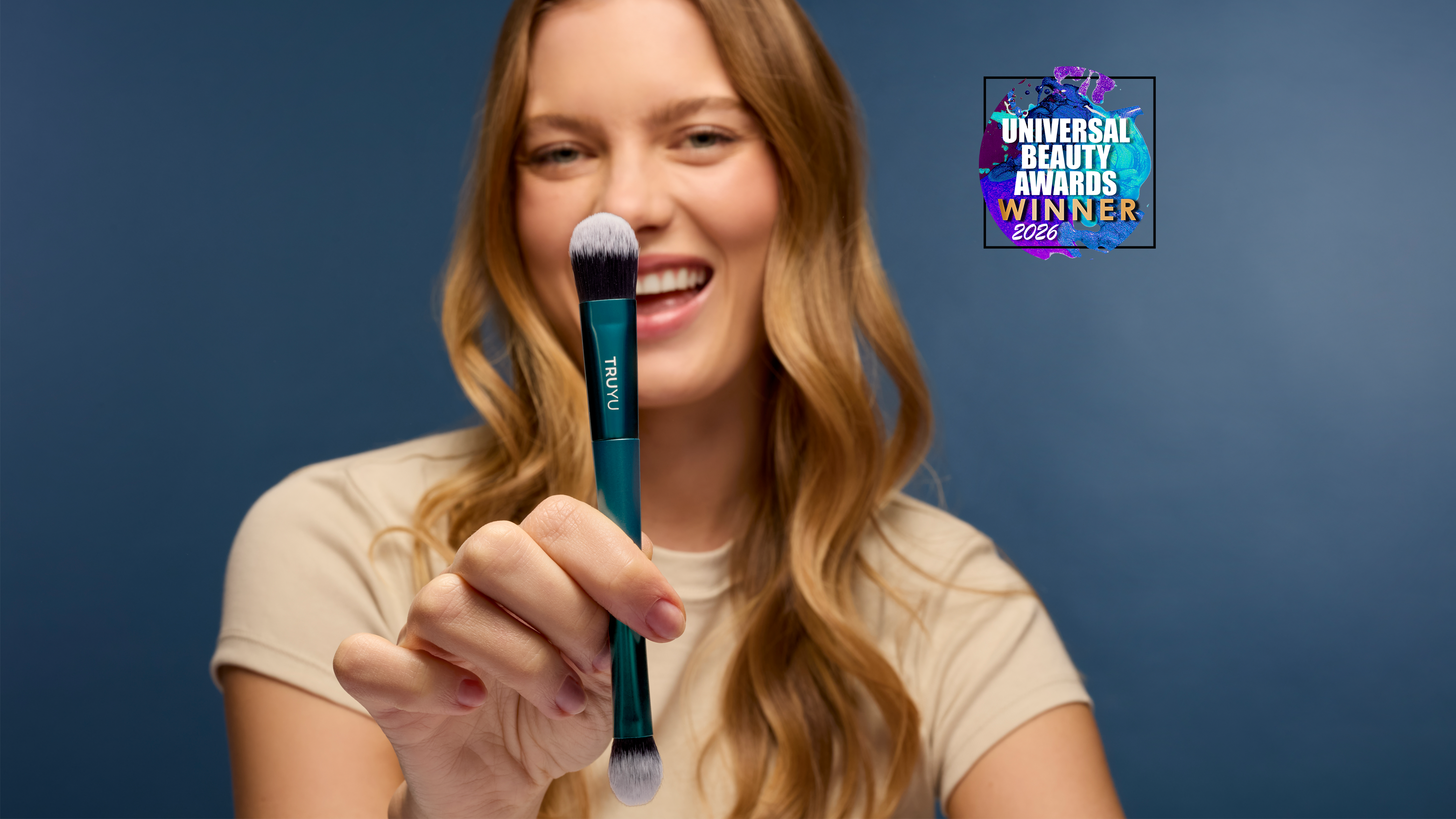 Model smiling, holding TRUYU Complexion Duo brush in front of face. 'Universal Beauty Awards Winner 2026' logo in top right corner. 