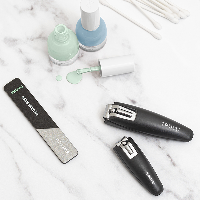 Lifestyle image of TRUYU Pro Manicure Set. Includes Nail Clipper, Toenail Clipper and Mini Buffer and Nail File out of pack on a marble background.