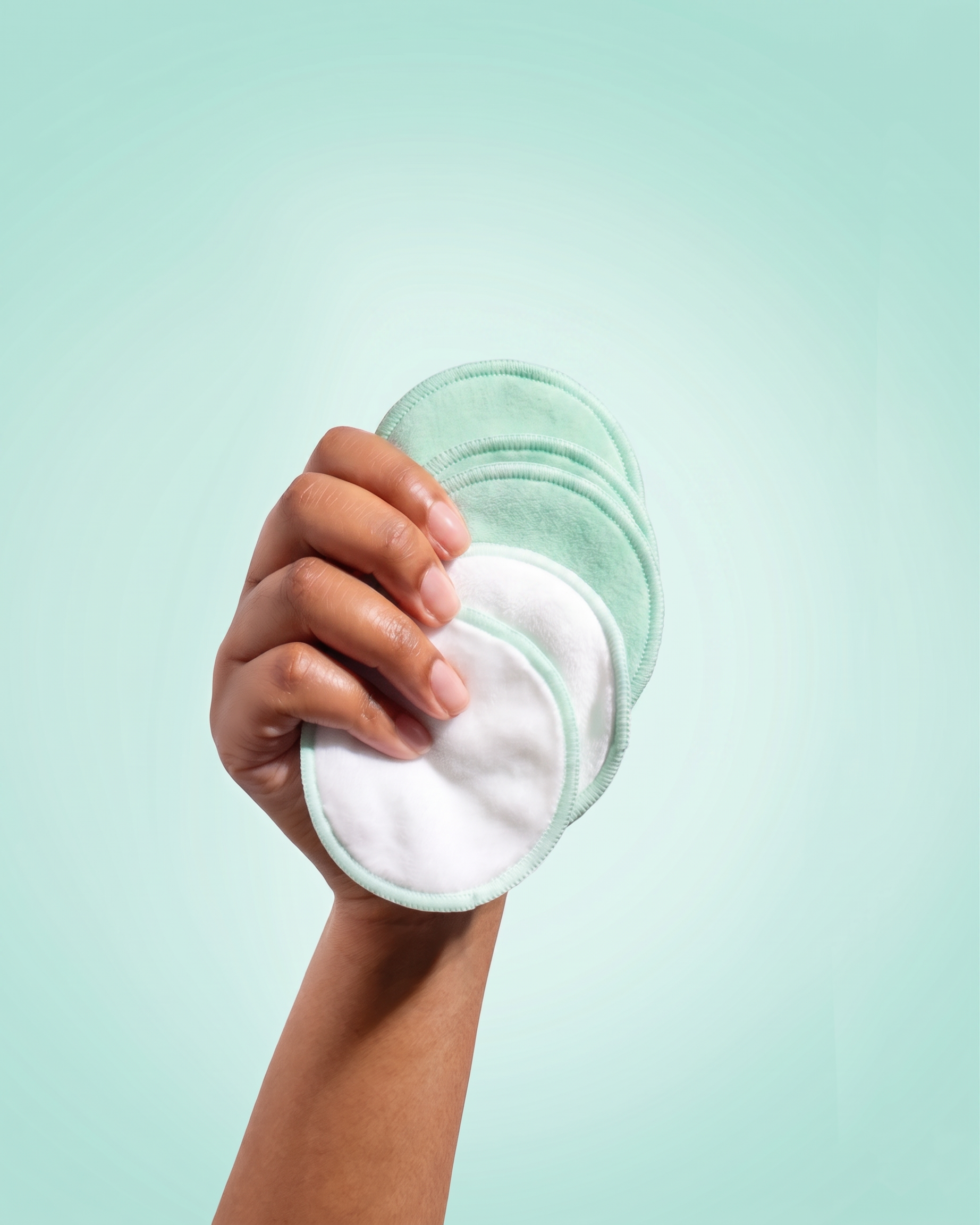 Hand holding five reusable makeup remover pads against a light blue background