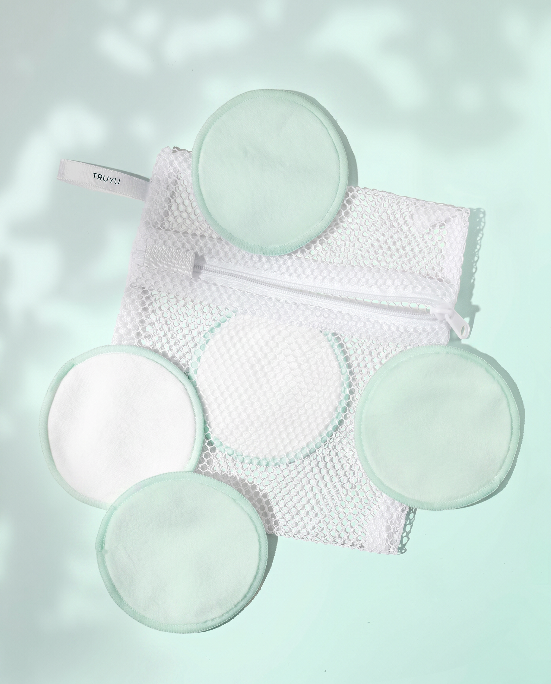Set of five reusable makeup remover pads and a mesh storage bag on a light green background