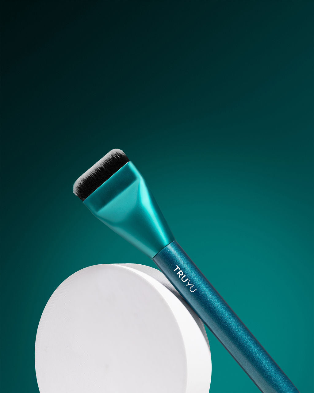 TRUYU Sculpting Brush propped against white circle plinth. On a teal background.