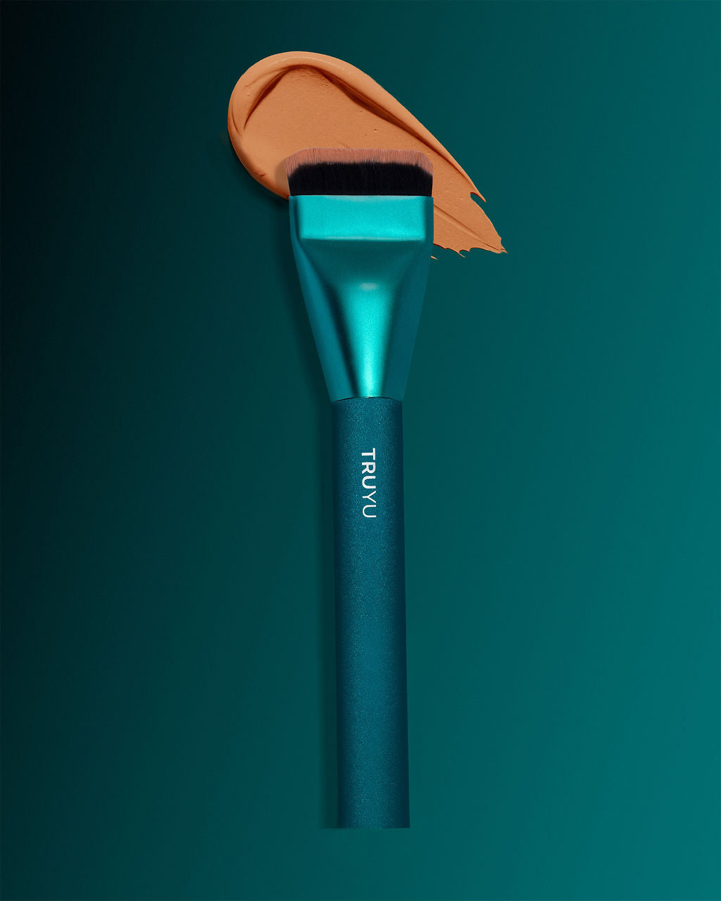 TRUYU Sculpting Brush with foundation swoosh behind bristles on a teal background.