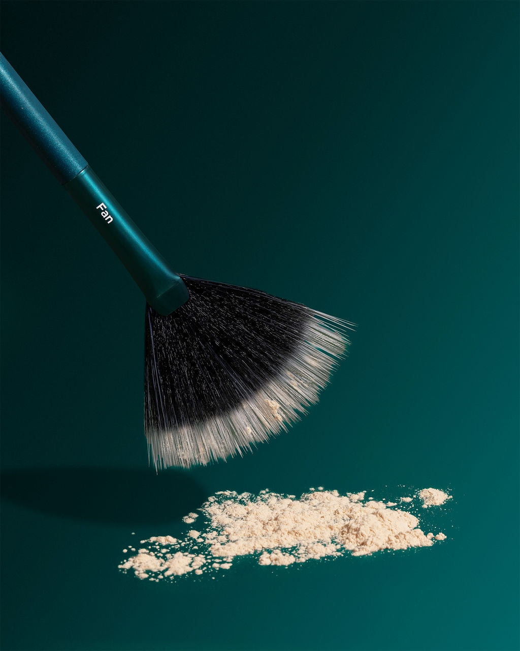 TRUYU Fan Brush hovering over cream powder on a teal background