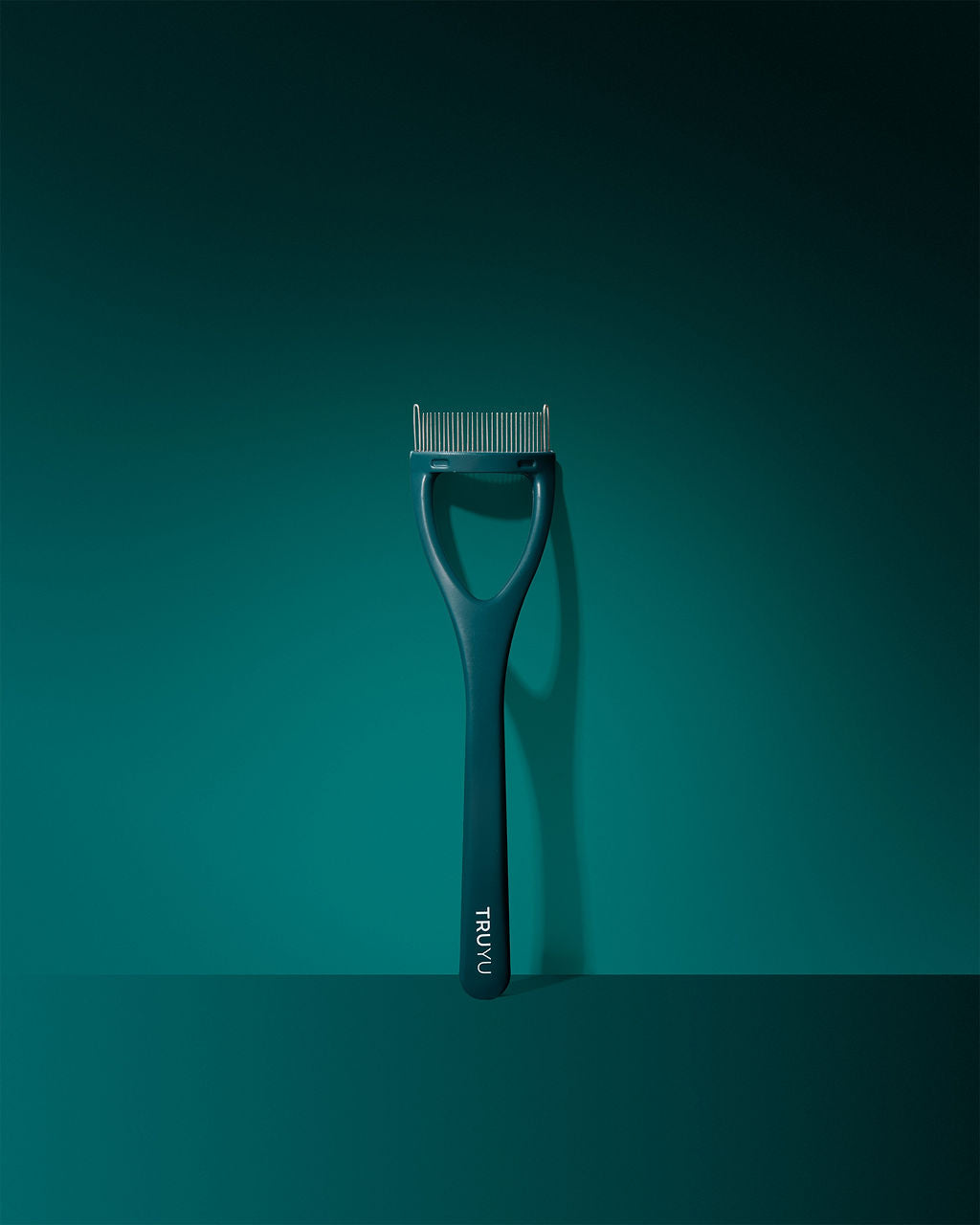TRUYU Eyelash Comb with 'TRUYU' logo on handle. Out of packaging, on a teal background
