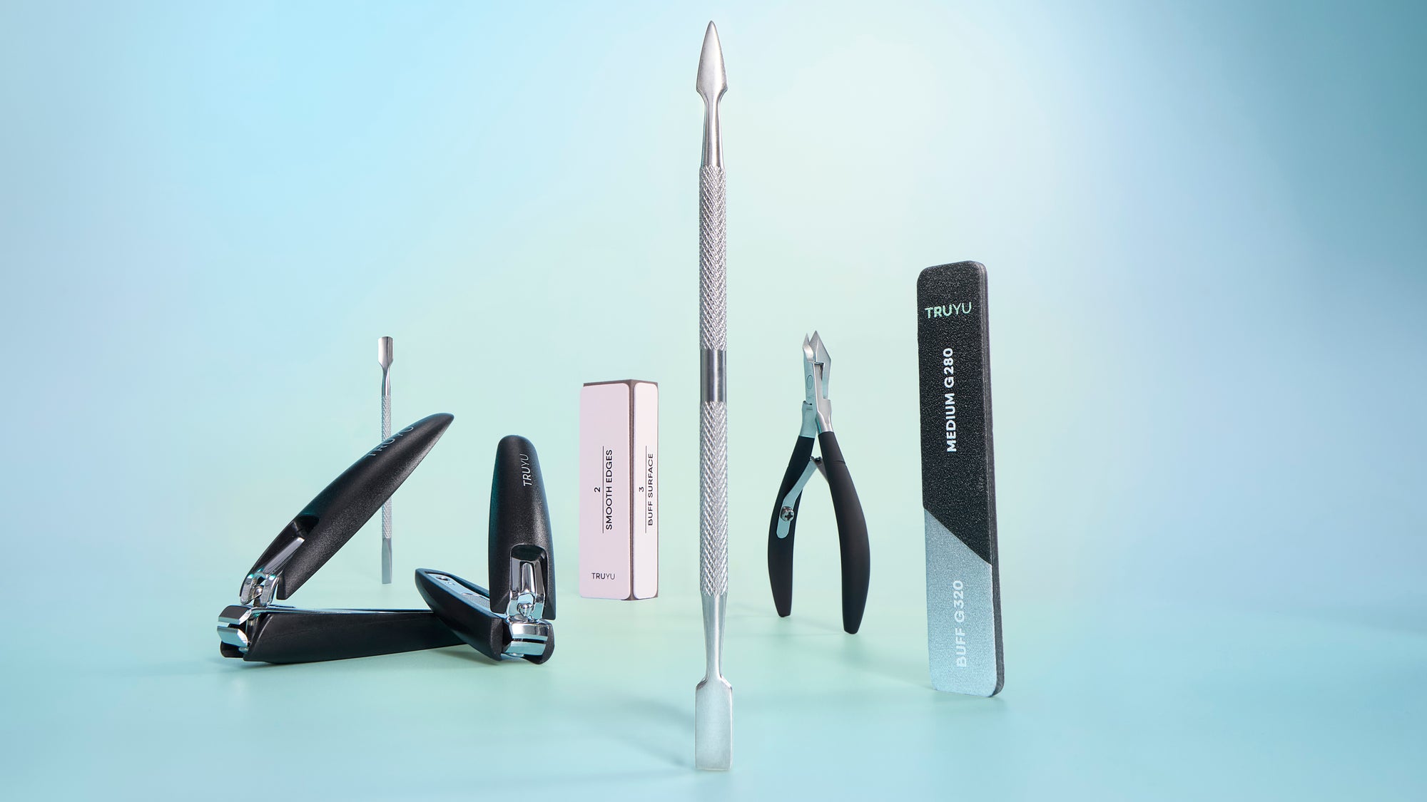 A set of nail care tools arranged on a light blue studio background, including black nail clippers, a black nail file, a silver metal nail file, a small pink box, and a black-and-silver rectangular tool.