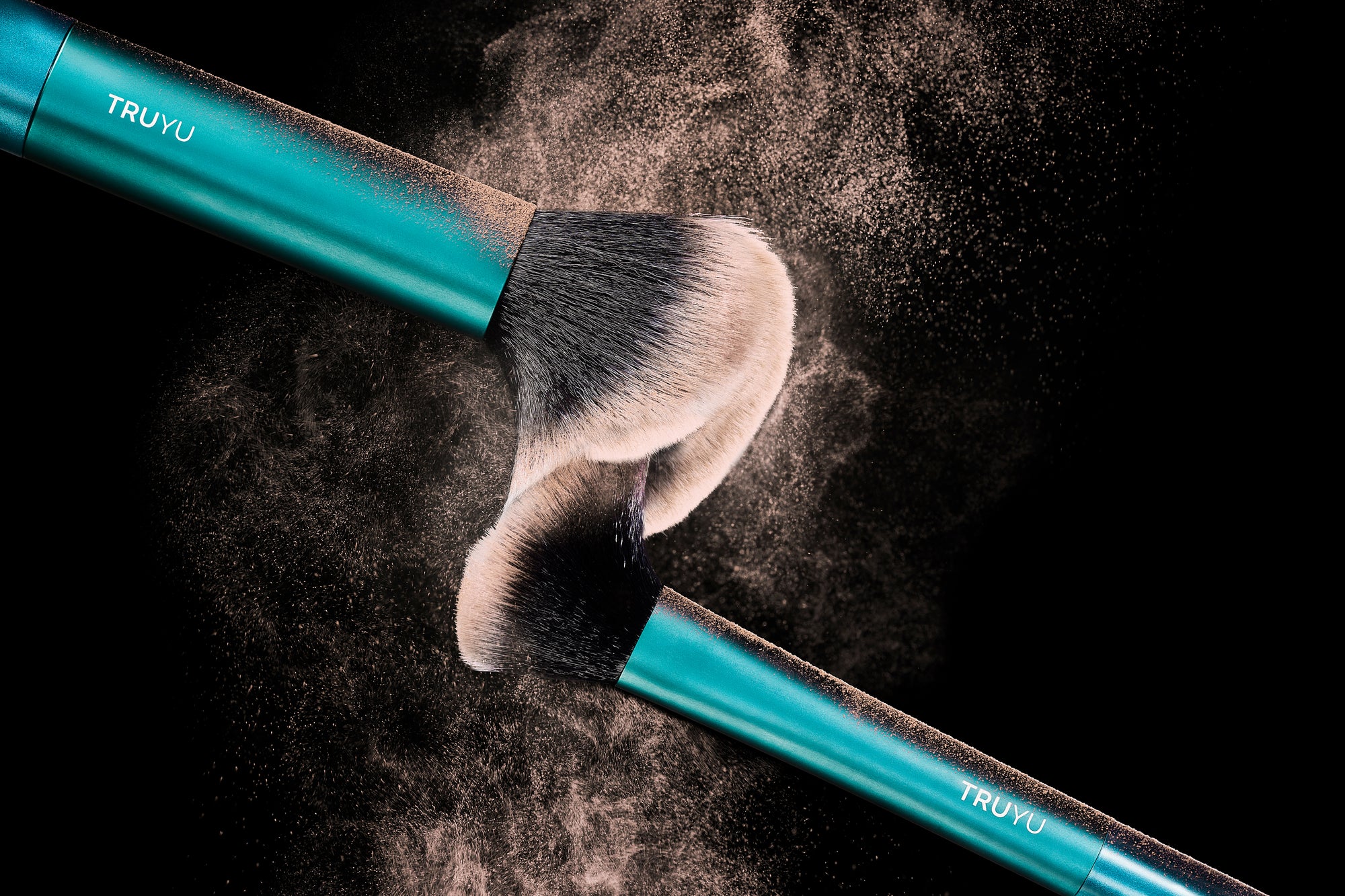 Two teal makeup brushes with black bristles and white-to-black gradient tips, shown against a black background with dramatic powder clouds. The handles are branded with the TRUYU logo.