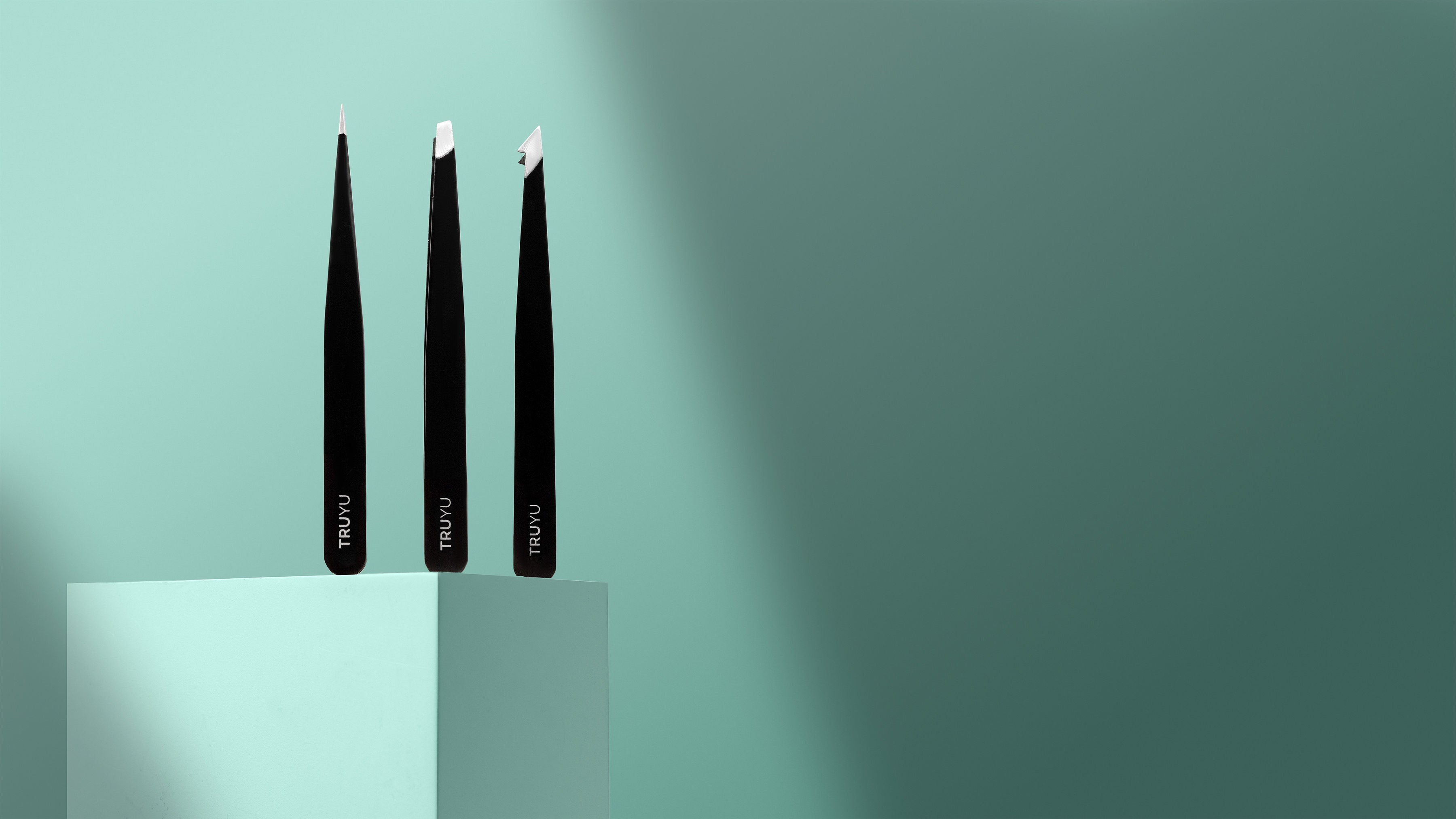 Three black eyelash extensions on a light blue platform with a gradient green background